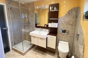 Moderni kylpyhuone, jossa on lasiseinällä varustettu suihku, valkoinen pesuallas ja wc.