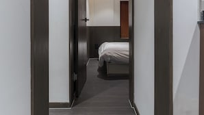 A narrow hallway with a dark wooden door leading to a bedroom with a bed and a nightstand. - J nine Lodge (Seoul)