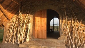 An arched wooden door leading into a room with a stone wall and a view of the outdoors.
