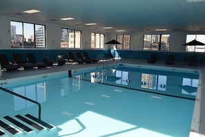 Una piscina interior con vistas despejadas de la ciudad gracias a amplios ventanales, tumbonas y sombrillas.