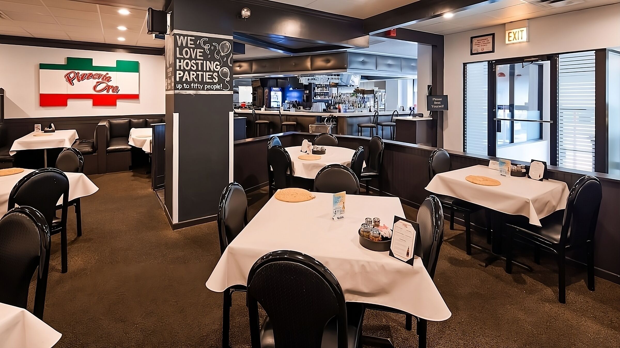 Een restaurant met tafels en stoelen, een bar en een bord waarop staat dat het vijftig personen kan verwelkomen.