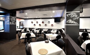 A restaurant interior with multiple tables and chairs, a wall with pizza-themed decorations, and a sign indicating 'Pizza Ora Chicago'.