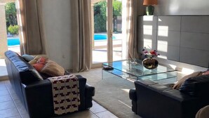 Un salon moderne avec une table basse en verre, deux canapés et une vue sur une piscine, visible à travers une porte-fenêtre coulissante.