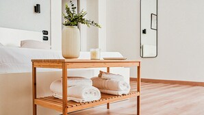 A neatly made bed with white linens, a wooden side table with towels, a vase with green plants, and a wall-mounted mirror. - 174 Urban Stay (Naples)