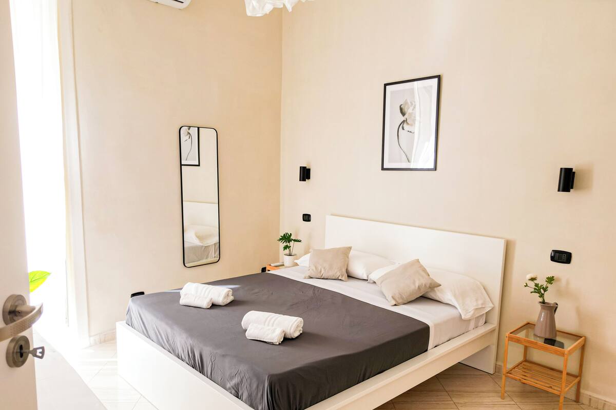 Une chambre d’hôtel moderne avec un grand lit, une table de chevet ornée d’un vase et un miroir fixé au mur.