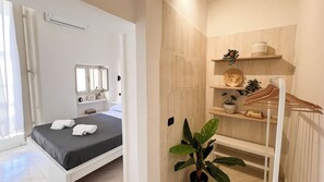 A bedroom with a bed, a bedside table, a mirror, a shelf with plants, and a hanging rack. - 174 Urban Stay (Naples)