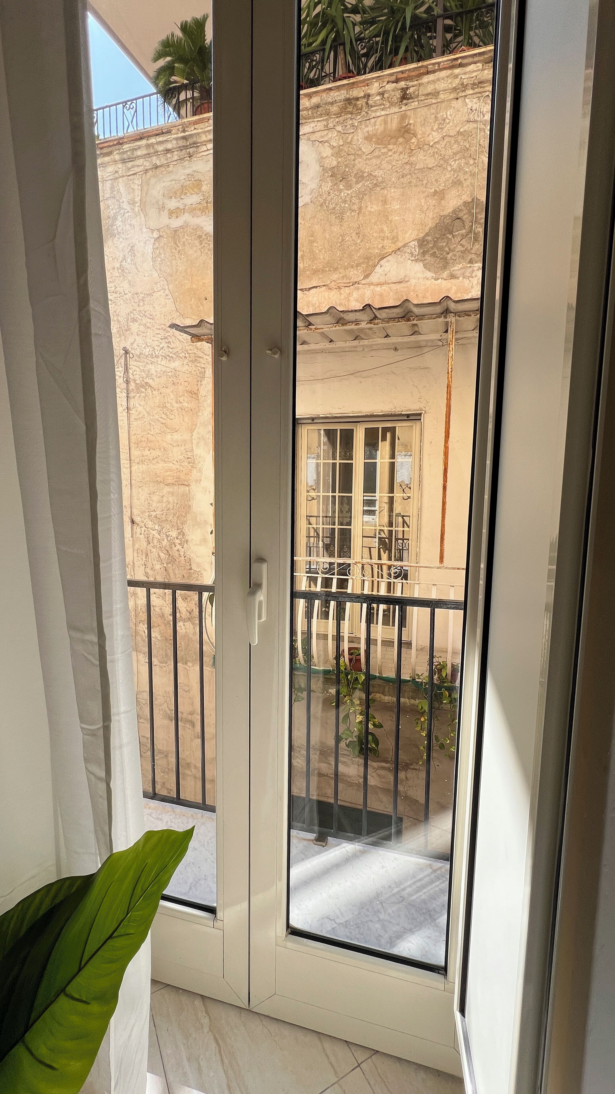 Uma varanda com vista para a fachada de um edifício, guarda-corpo de metal e um vaso com planta.