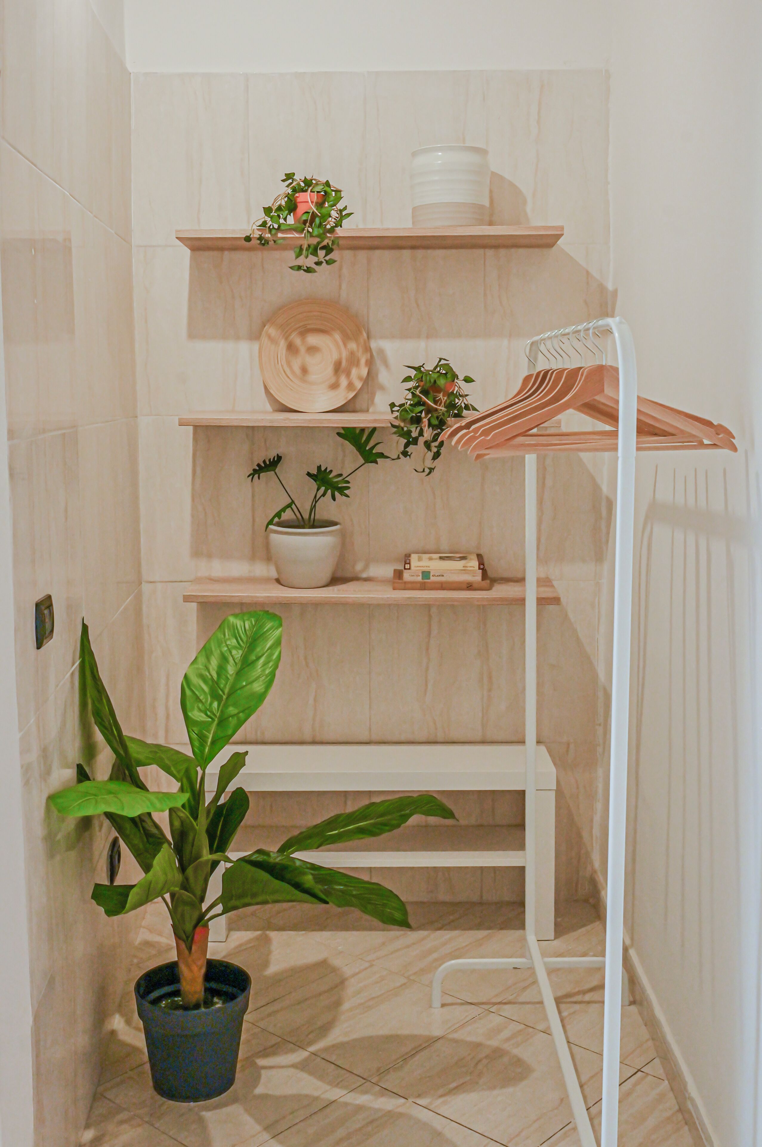 A bathroom with a white tiled floor, a wooden shelf with a potted plant, a white radiator, and a white towel rack.