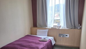 A hotel room with a bed, a desk, a window with curtains, and a wall-mounted air conditioner. - Kanonji Grand Hotel (Kanonji)