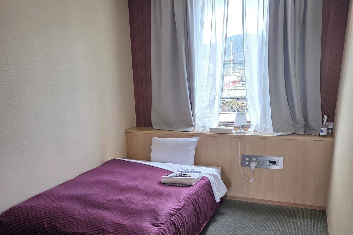 A hotel room with a bed, a desk, a window with curtains, and a wall-mounted air conditioner.