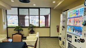 A hotel room with a dining area, a bonsai tree, a vending machine, and a view of the street outside. - Kanonji Grand Hotel (Kanonji)