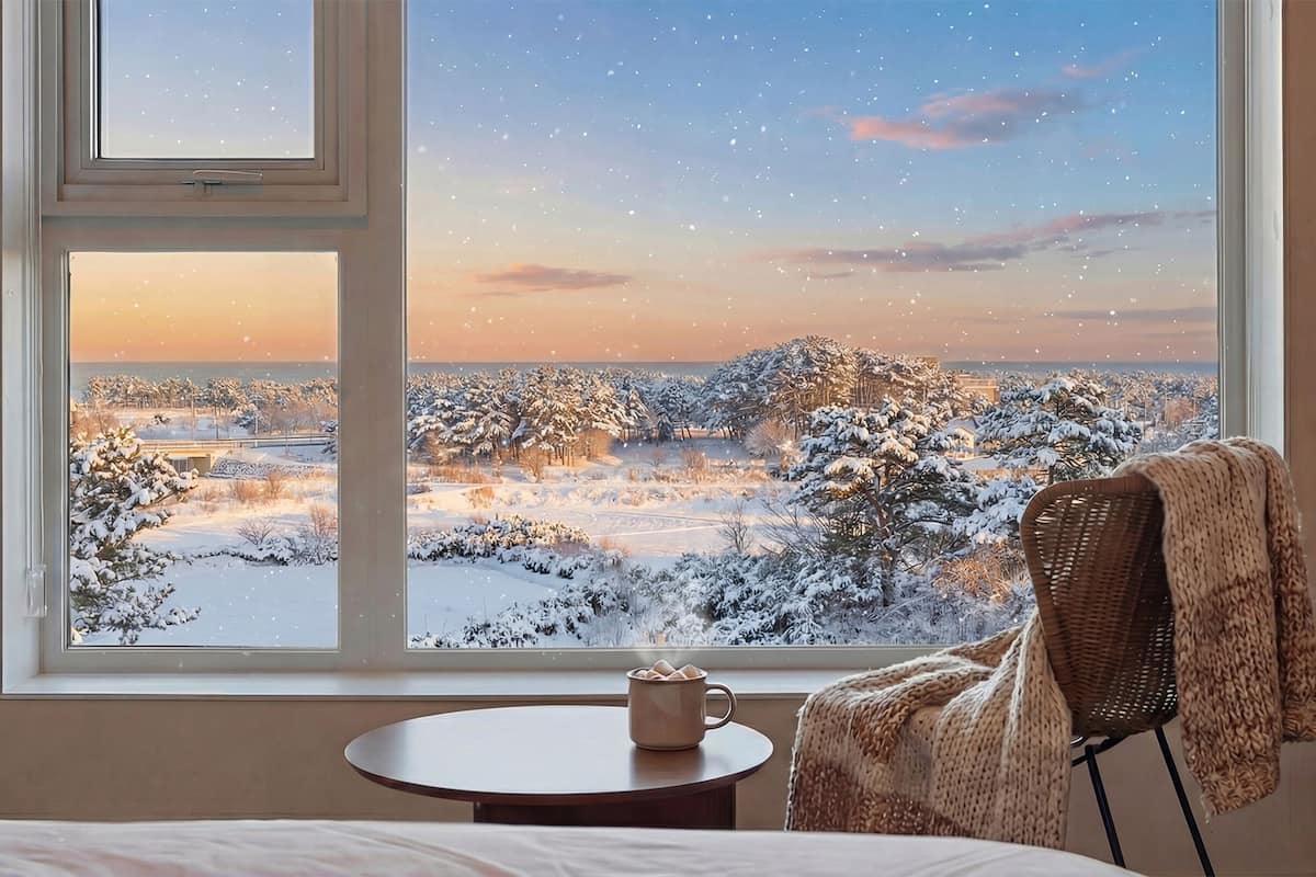 A room with a large window offering a view of a snowy landscape during sunset.