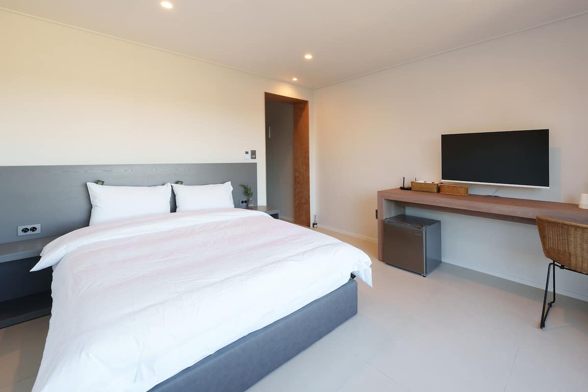 A modern hotel room with a large bed, a desk with a flat-screen TV, a coffee maker, and a small refrigerator.