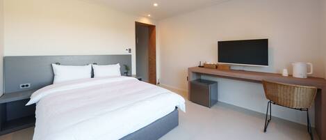 A modern hotel room with a large bed, a desk with a flat-screen TV, a coffee maker, and a small refrigerator.