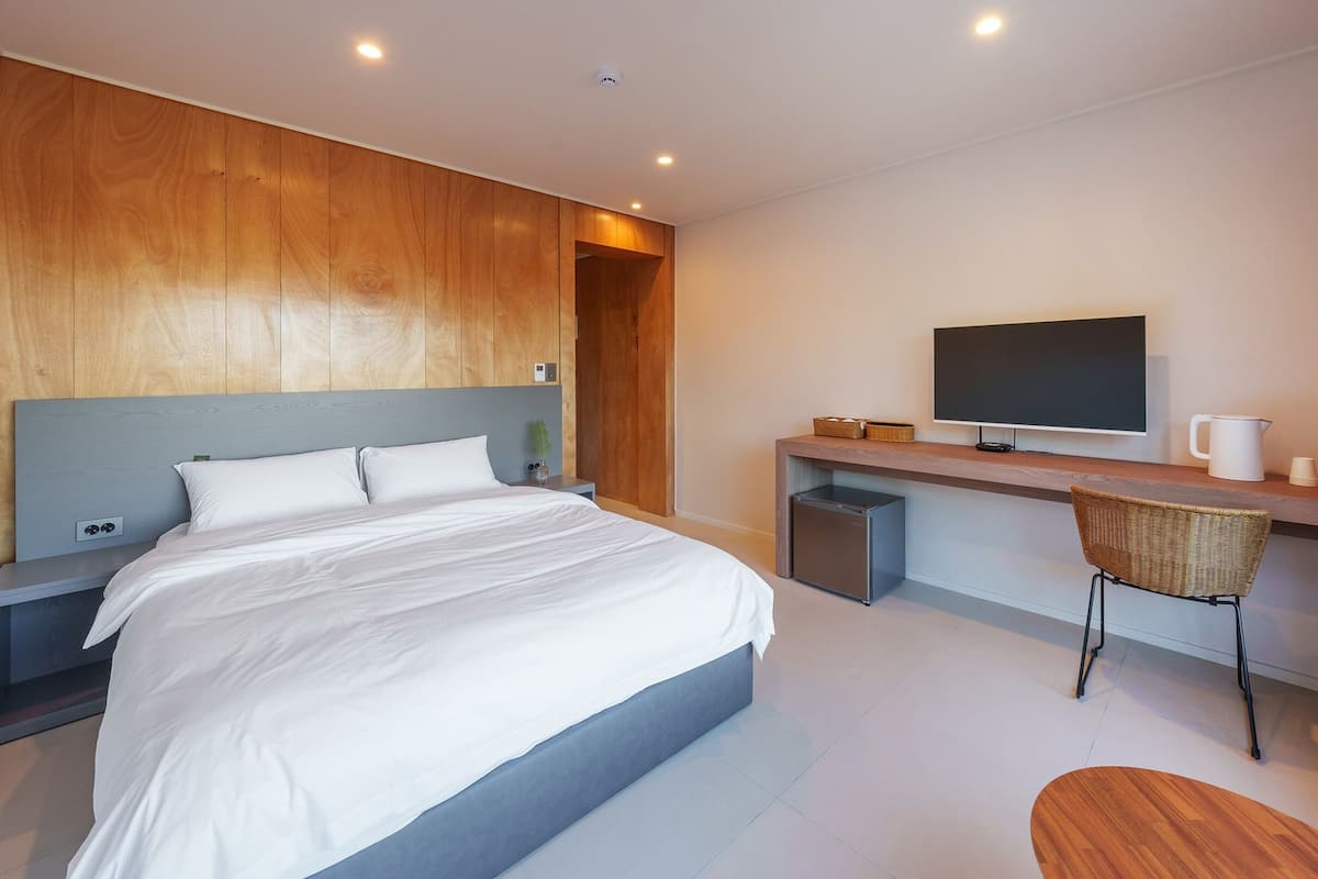 A modern bedroom with a bed, a desk, a chair, and a television.