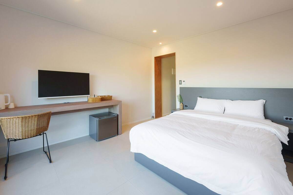 A modern hotel room with a large bed, a desk with a flat-screen TV, a chair, and a nightstand.
