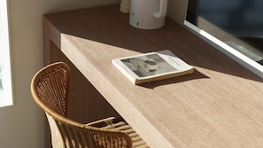 A wicker chair at a wooden table with a book and a white object, possibly a coffee maker, in the background. - Yangyang Stay Y (Yangyang)
