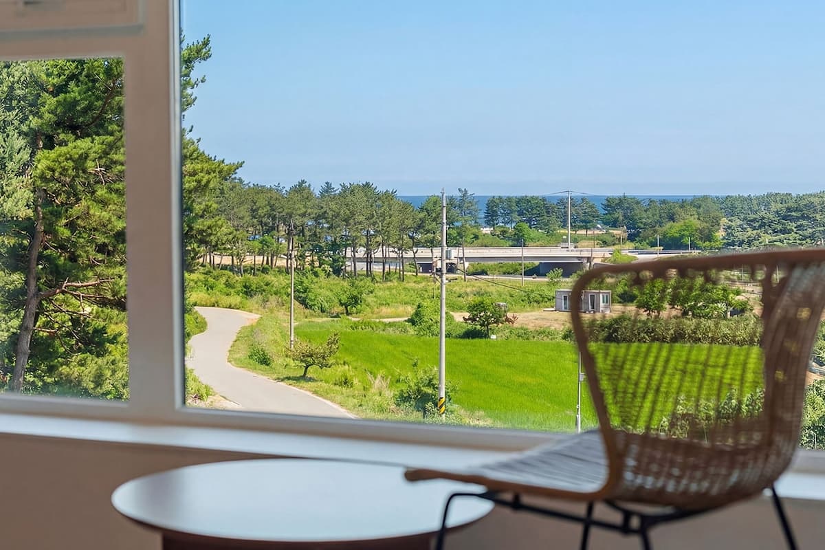 A room with a view of a winding road through a green landscape, a chair, and a small table.