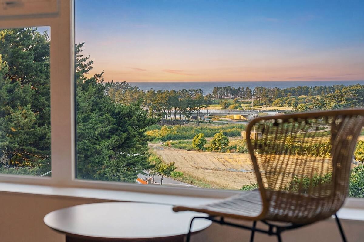 A room with a large window overlooking a forested area and a bridge.