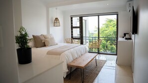 Une chambre moderne avec un grand lit, un banc, une plante en pot et un balcon donnant sur un paysage verdoyant.