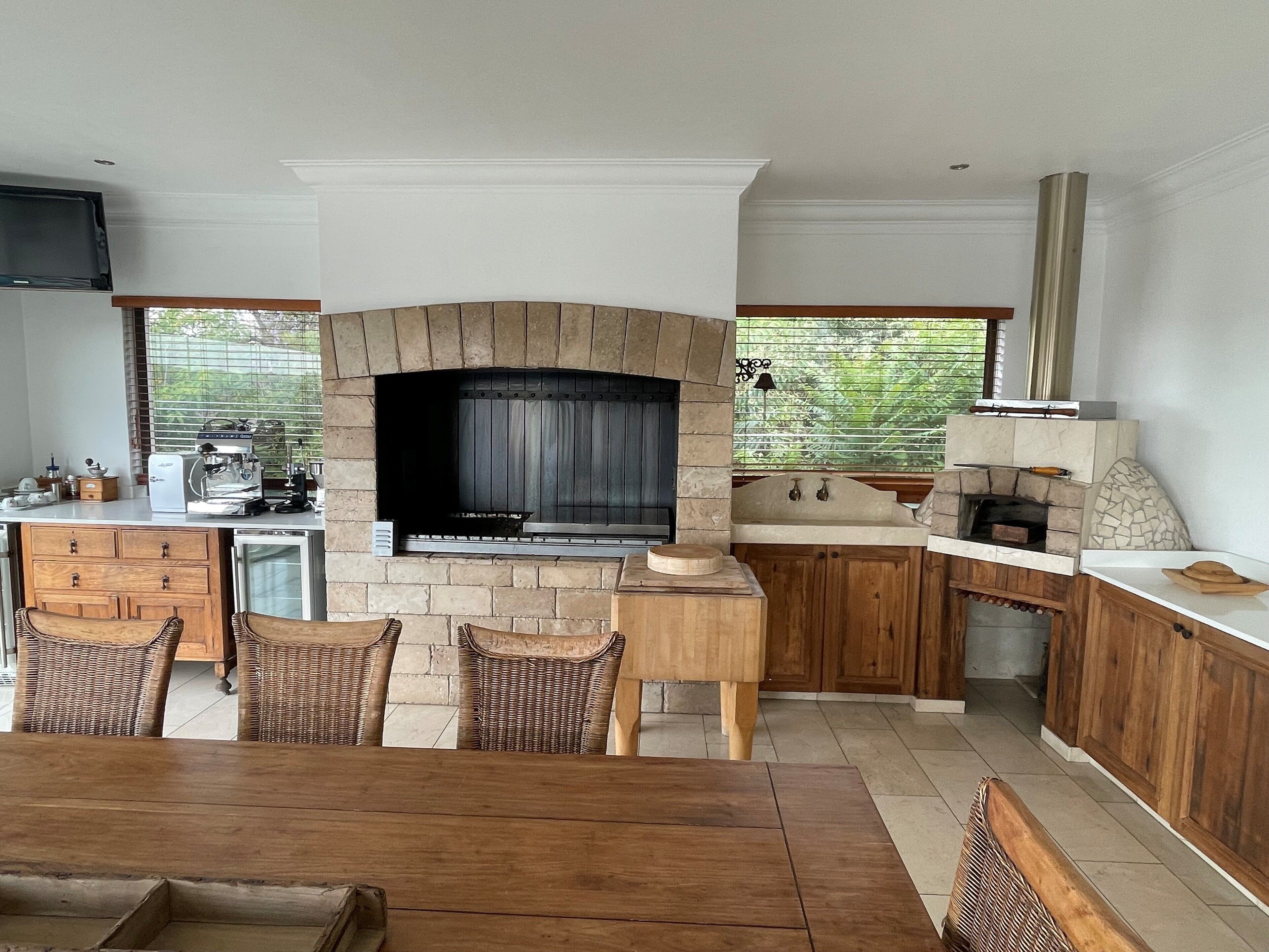 A modern kitchen with a stone fireplace, wooden cabinets, and a dining area with wicker chairs.
