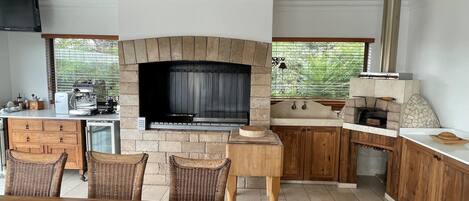A modern kitchen with a stone fireplace, wooden cabinets, and a dining area with wicker chairs.