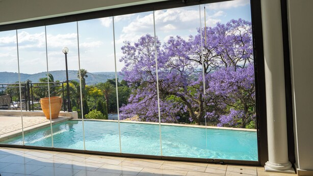 Un espace piscine offrant une vue sur des arbres aux fleurs violettes et sur des montagnes lointaines.