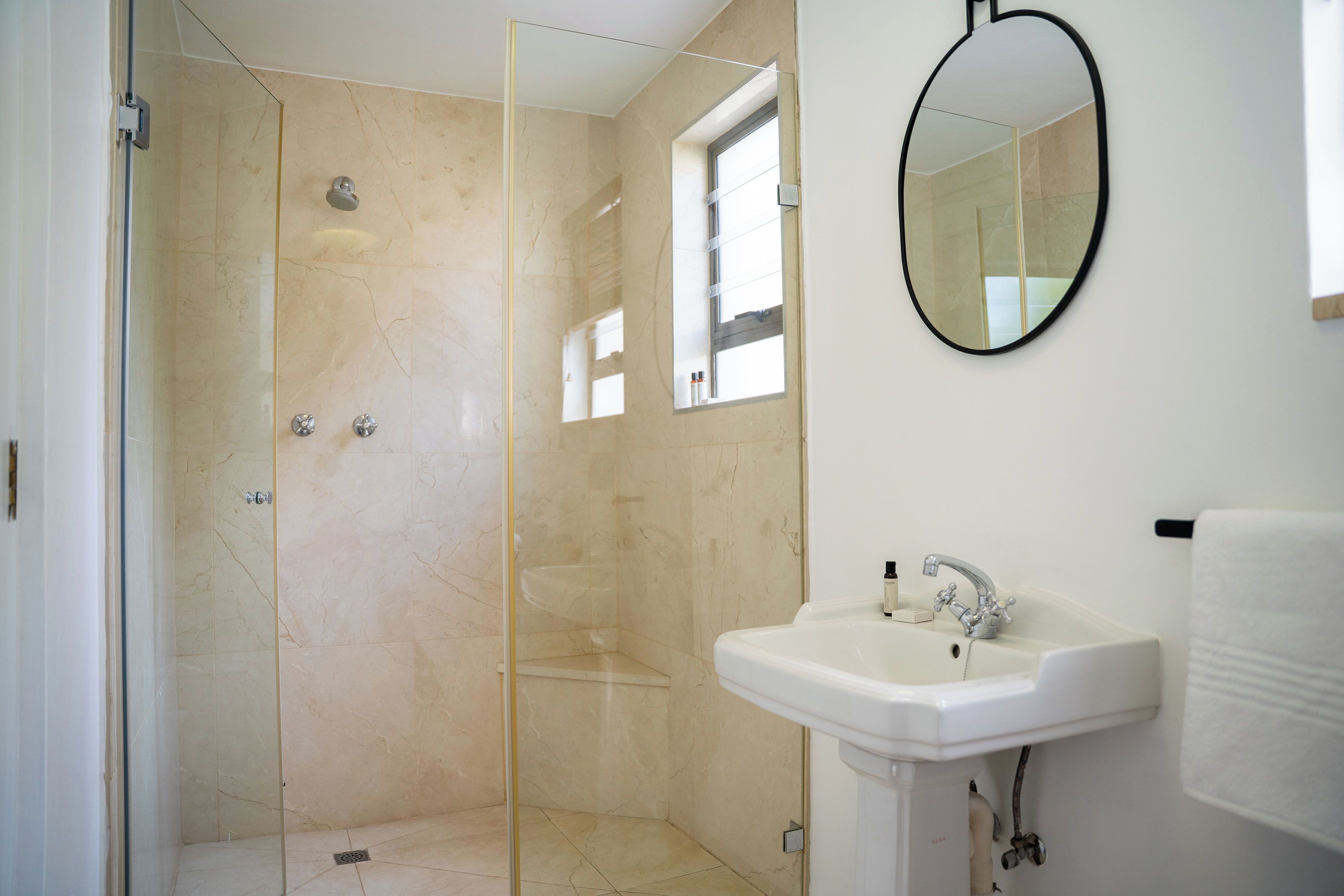 A modern bathroom with a glass-enclosed shower, a white sink, and a mirror on the wall.