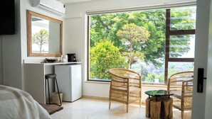 Une chambre d’hôtel avec une grande fenêtre, des meubles en osier, une petite table et une armoire blanche.