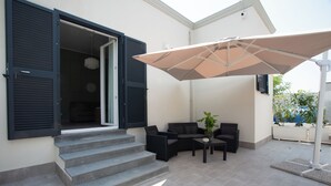 Un patio con mobiliario exterior, una planta en maceta y un paraguas grande.