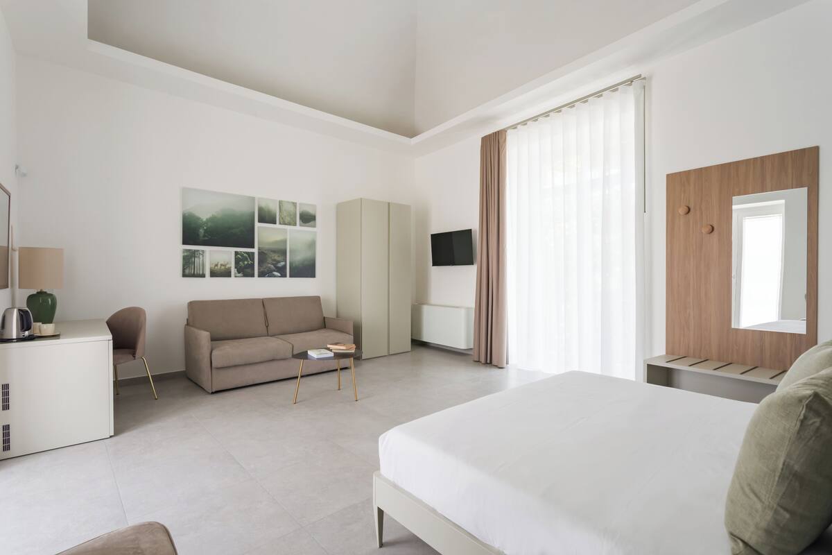 Ein modernes Hotelzimmer mit einem großen Bett, einer Couch, einem Schreibtisch und einem Fernseher.