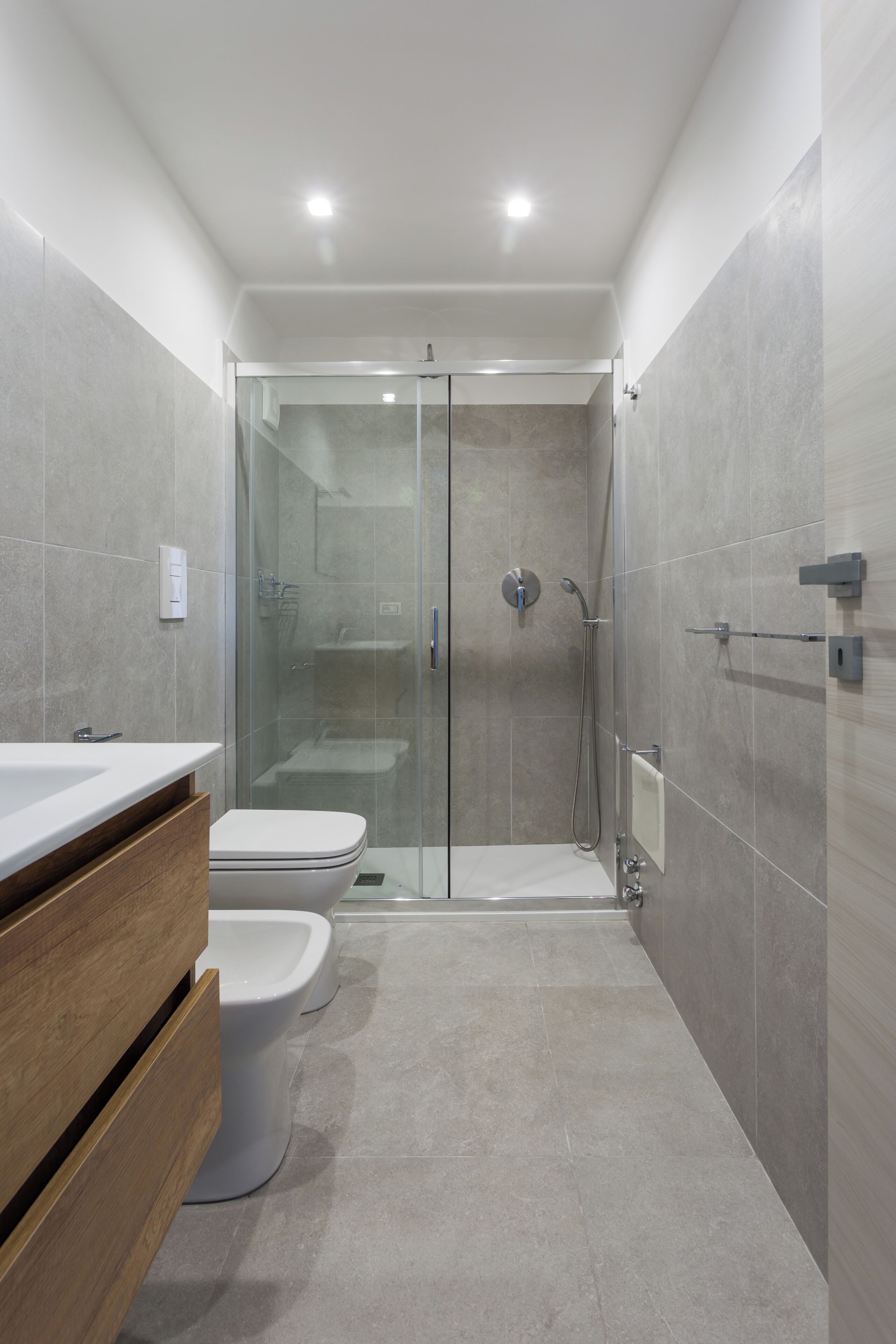 Un baño moderno con ducha de vidrio, tocador de madera y un inodoro blanco.