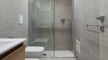 Un baño moderno con ducha de vidrio, tocador de madera y un inodoro blanco.