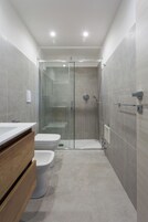 Un baño moderno con ducha de vidrio, tocador de madera y un inodoro blanco.