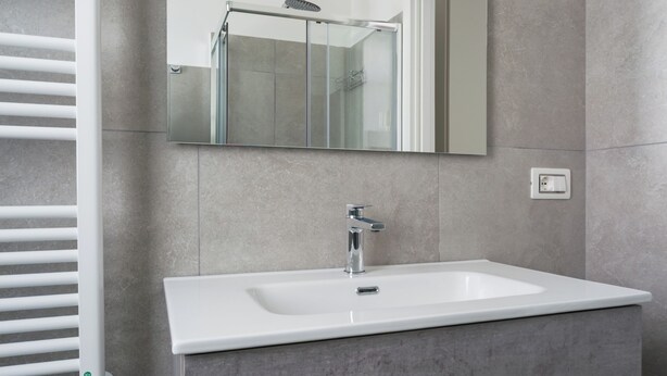 A modern bathroom with a white sink, a mirror above it, and a towel rack to the left. - Palazzo Vesuviano (Terzigno)