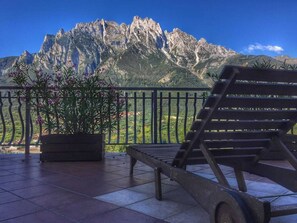 A balcony with a mountain view, a potted plant, and a lounge chair.