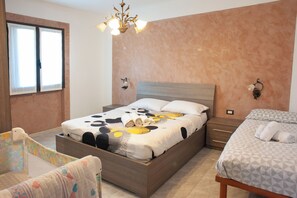 Quarto com uma cama grande, uma cama menor, mesa de cabeceira, cadeira, janela e lustre.