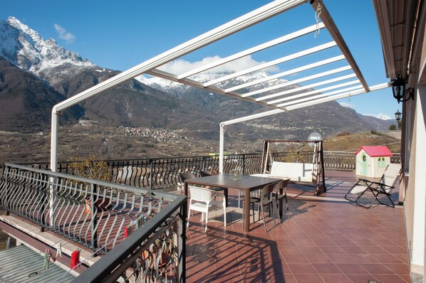 A terrace with a table and chairs, a small playhouse, and a view of snow-capped mountains.