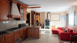 A modern kitchen with wooden cabinets, a gas stove, and a built-in oven. There is a red sofa and a dining table in the living area.
