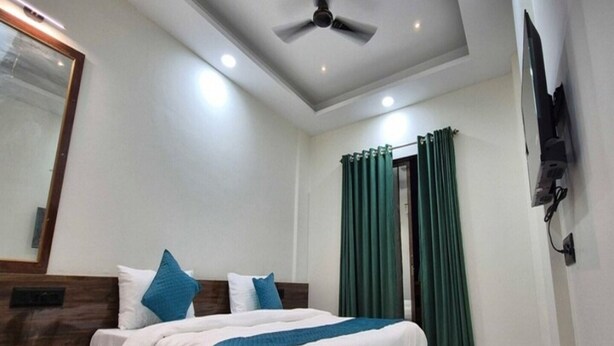 A hotel room with a bed, a ceiling fan, a TV mounted on the wall, and green curtains. - Townhouse Oak Pawana Road Lonavala (Mawal)