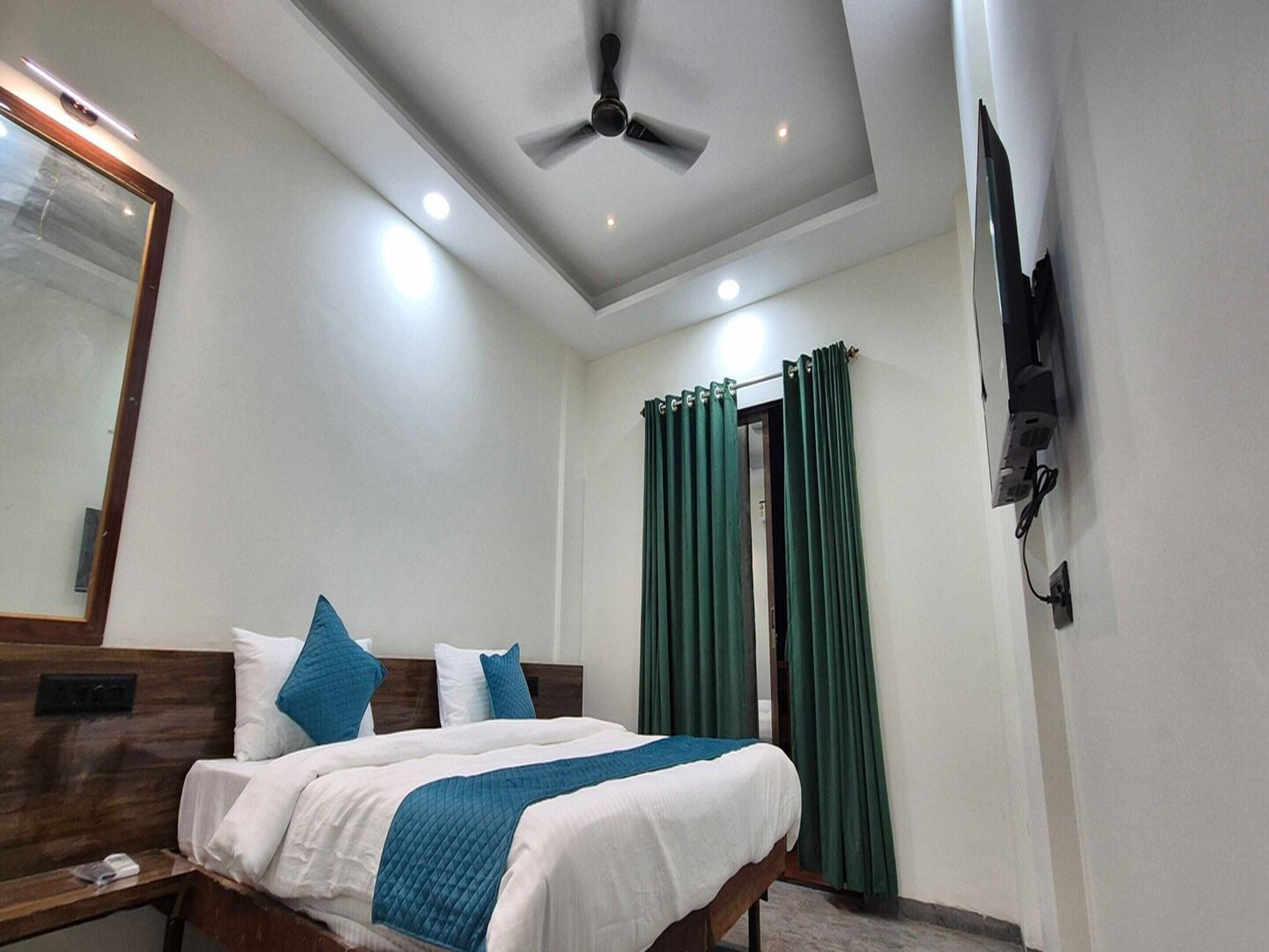 Una habitación de hotel con una cama, ventilador de techo, televisión montada en la pared y cortinas verdes.