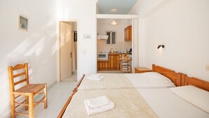 Een kamer met twee bedden, een houten stoel, een klein tafeltje en een kitchenette op de achtergrond.