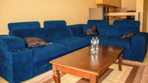 A blue sofa with a wooden coffee table in a living room with a kitchen in the background. - Elegant Stay near two rivers mall, Ruaka. (Ruaka)