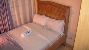 A neatly made bed with a wooden headboard, white bedding, and a rolled towel with "The Moon" logo. - Elegant Stay near two rivers mall, Ruaka. (Ruaka)
