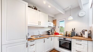 A modern kitchen with white cabinets, a wooden countertop, a built-in oven, and a window with a view. - Charming Schlei Cottage Lorenz – Nature Retreat for Up to 4 Guests (Boren)