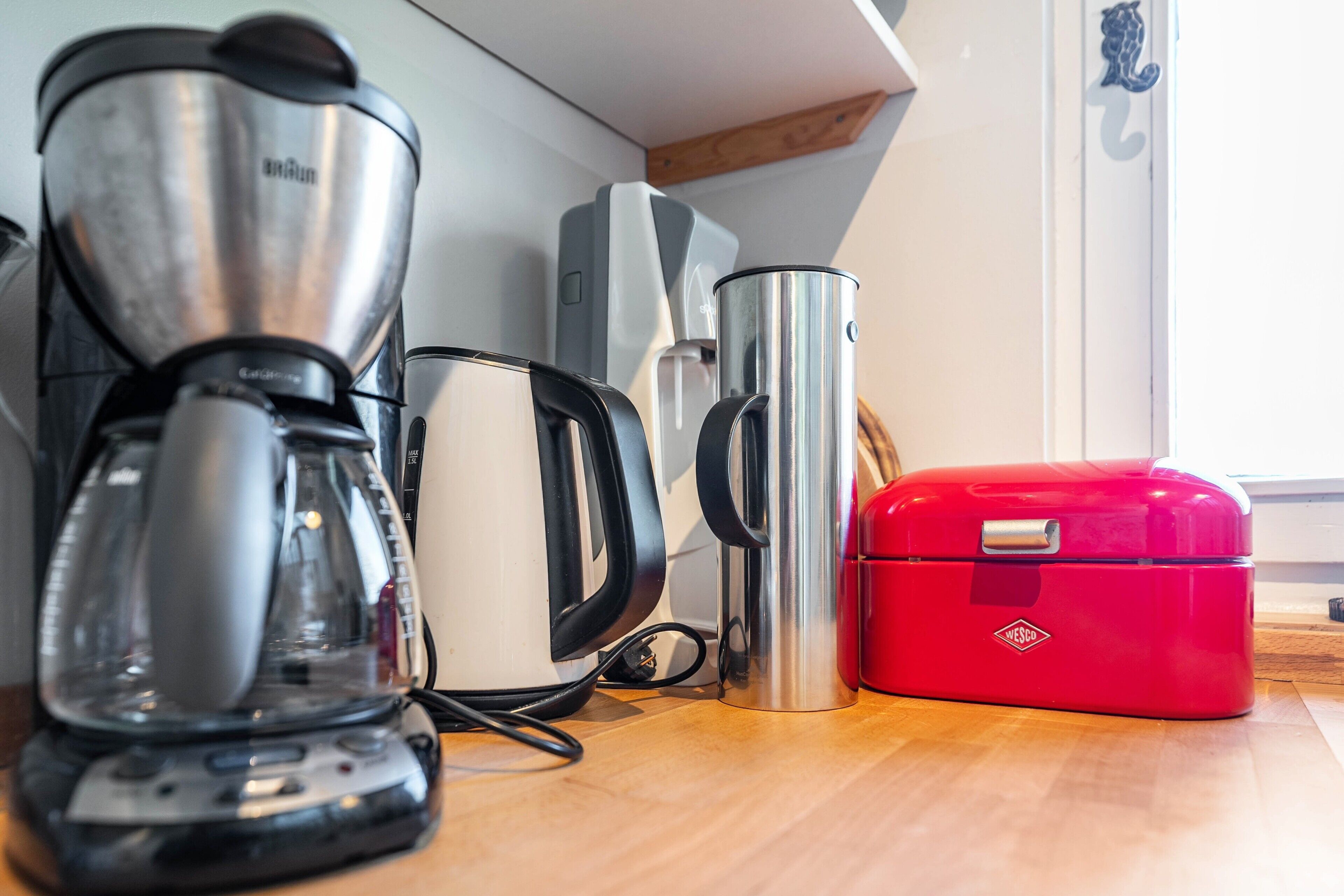 Une cuisine équipée d’une machine à café, d’une bouilloire et d’une boîte de rangement rouge.