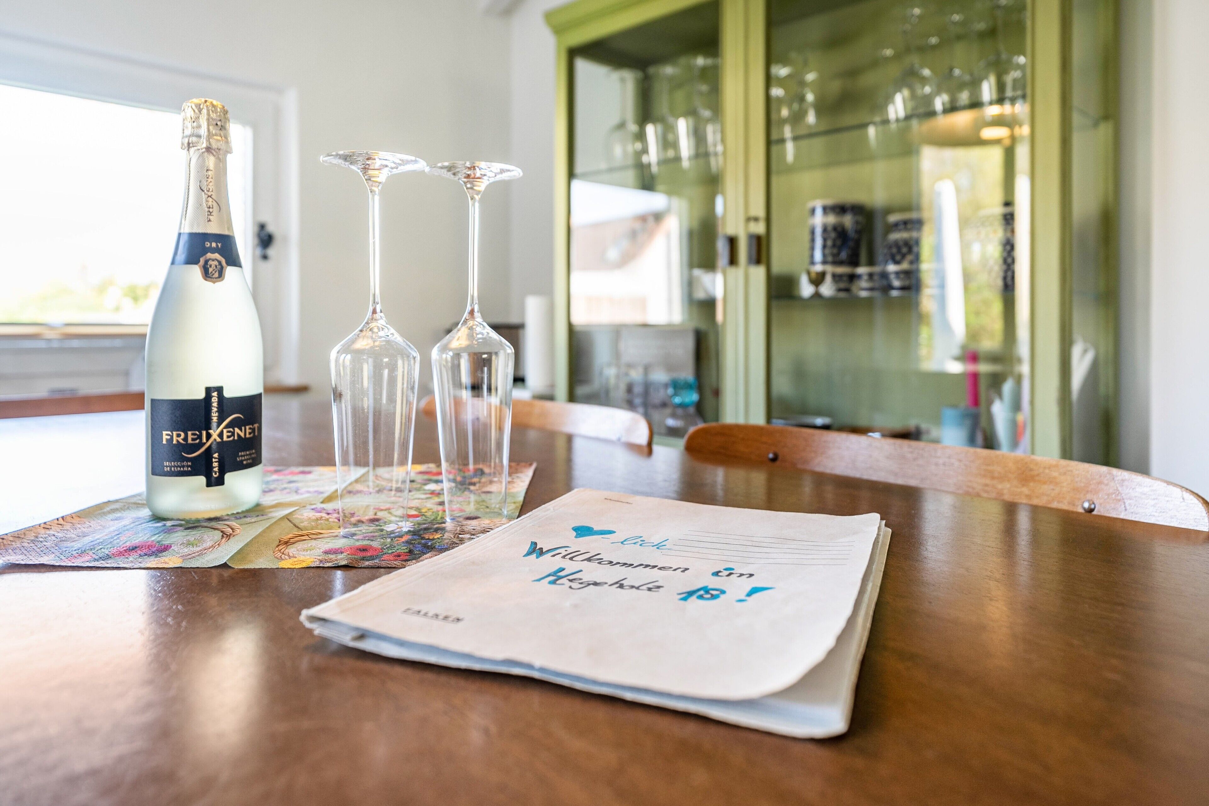 Een fles Freixenet champagne, twee wijnglazen en een menukaart op een houten tafel.