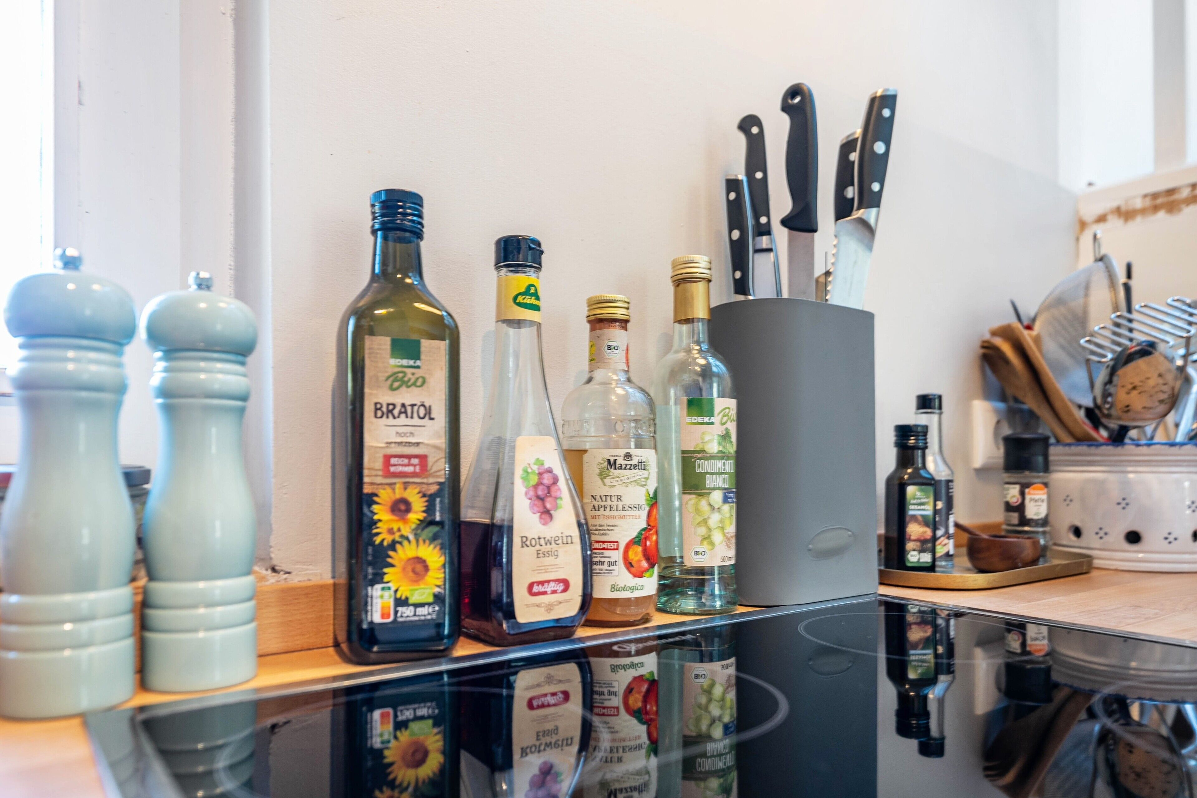 A kitchen counter with various bottles of condiments and cooking oils, a set of knives, and salt and pepper shakers.