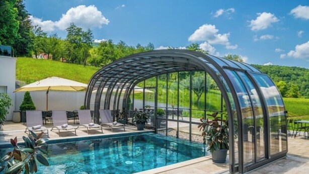 Lasiseinöin varustettu uima-allasalue, jossa on aurinkotuoleja ja pergola.