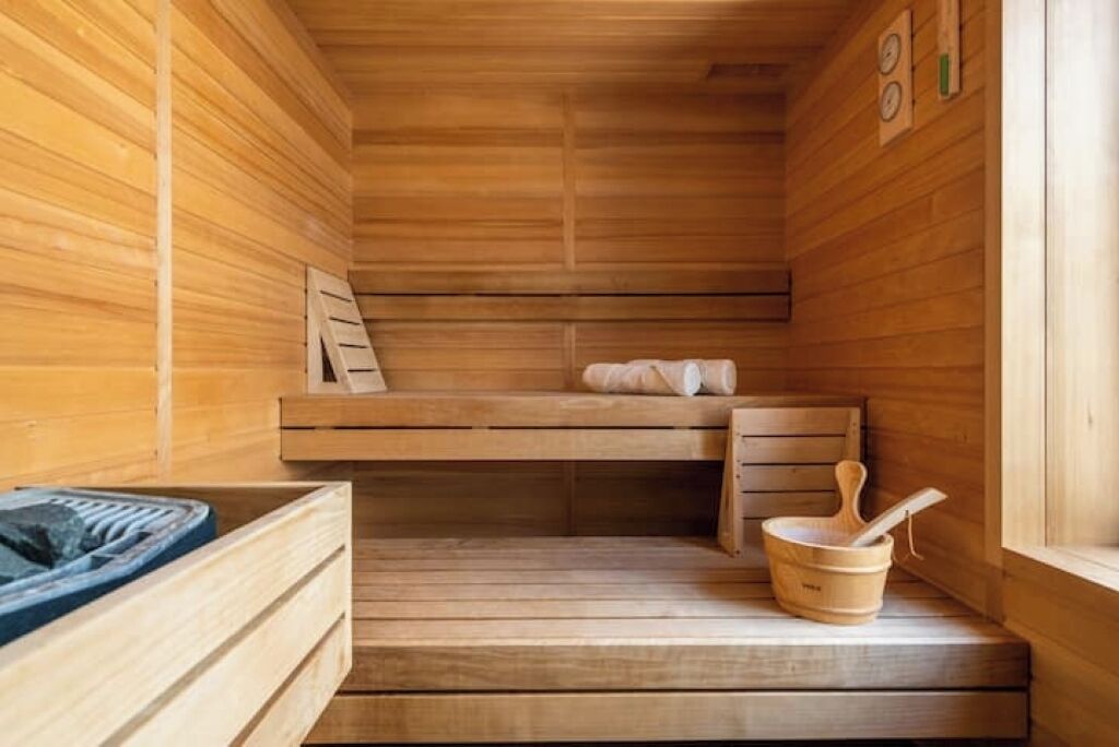 Un sauna avec des murs en bois, un banc, une petite table et un seau avec une brosse.